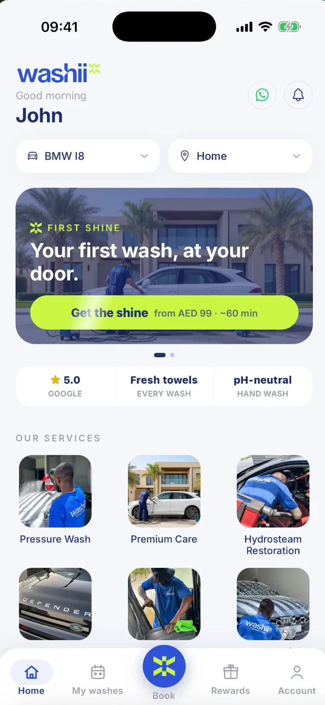 The app home screen: a greeting for John with his BMW i8 and home address already picked, a First Shine card offering a first wash at the door from AED 99, badges for a 5.0 Google rating, fresh towels and a pH-neutral hand wash, then the service tiles - Pressure Wash, Premium Care and Hydrosteam Restoration.